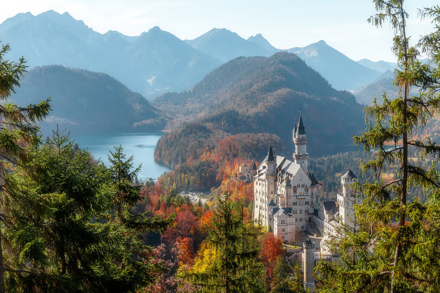 uitzicht op bergen, bossen en een meer met een groot kasteel op de voorgrond