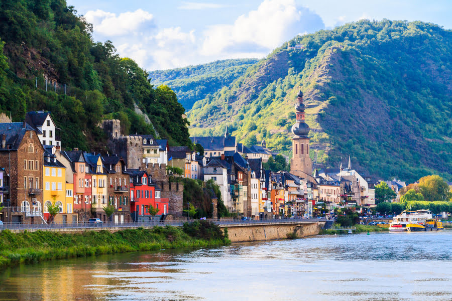 vakwerkhuizen en een kerkje aan een rivier met bergen op de achtergrond